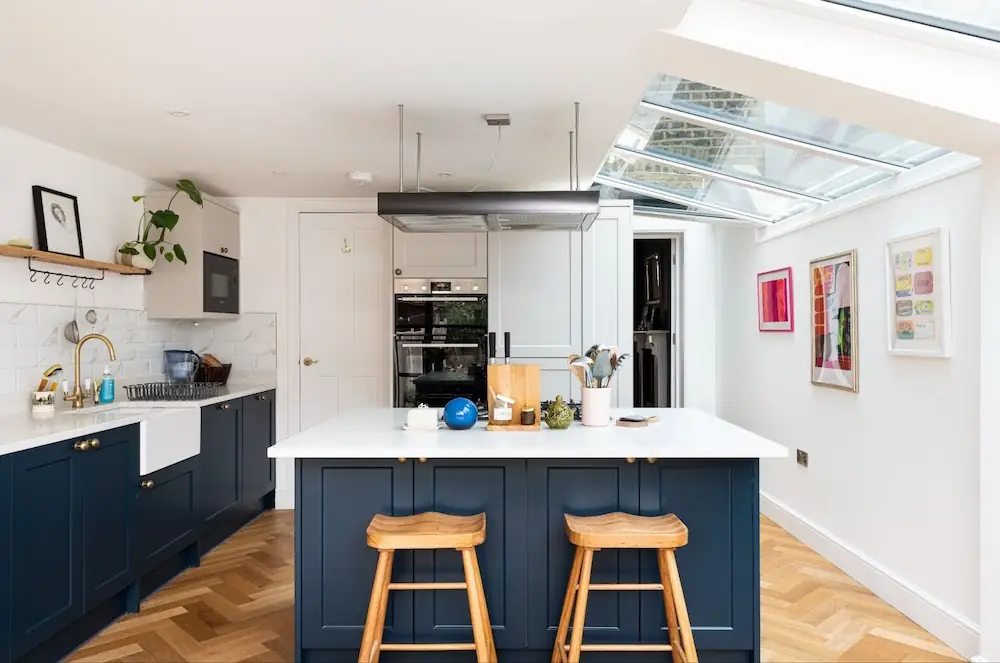 Bright kitchen with a dark blue island, timber stools and roof glazing