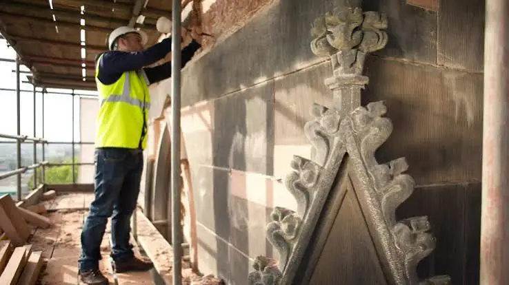 Tradesperson working on decorative stonework from scaffolding
